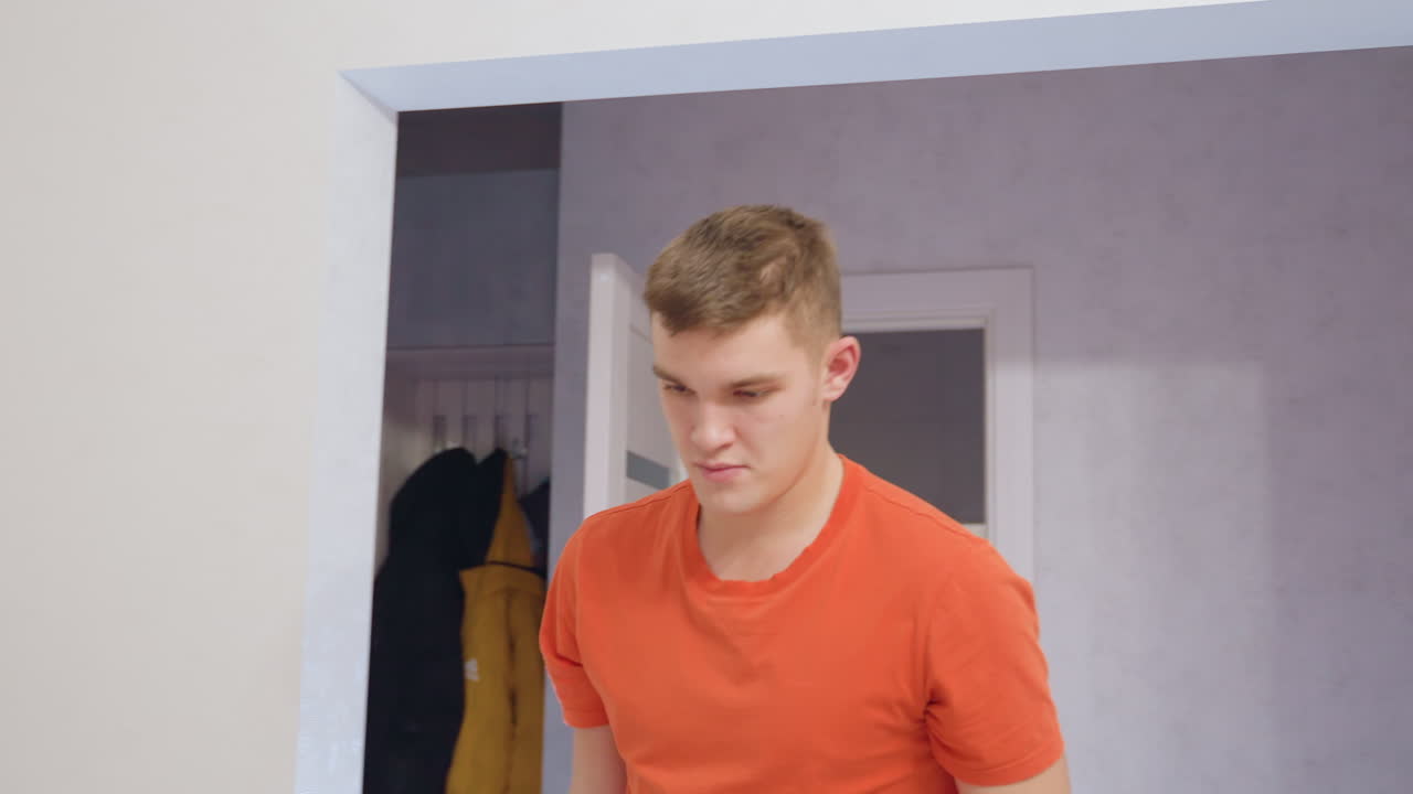 Gros plan sur un jeune homme en t-shirt orange, concentré sur sa routine de nettoyage alors qu’il se prépare en portant un seau, en le posant et en sortant un chiffon jaune pour essorer l’eau pour l’entretien du sol.