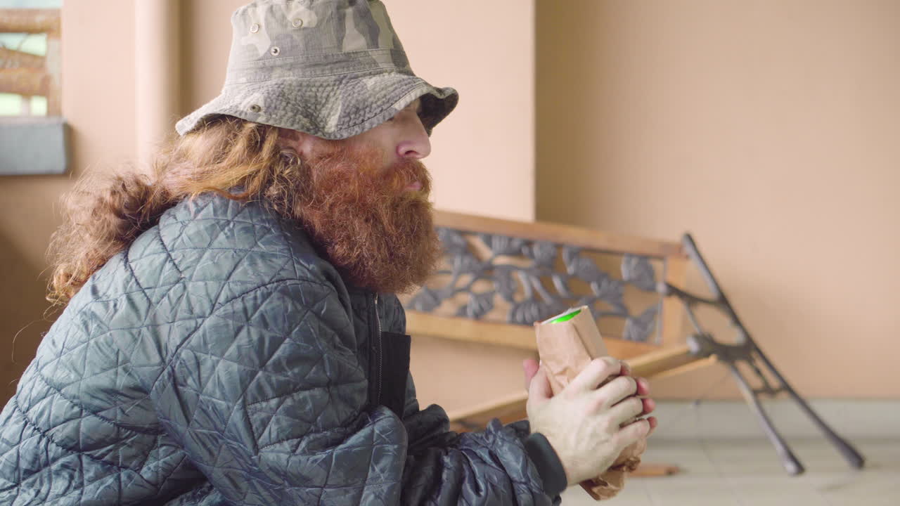 Homeless Man candidly looking around with beer can in hands outdoors near broken bench