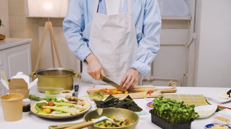 Homme japonais coupant des ingrédients dans la cuisine, puis regardant la caméra et souriant 1