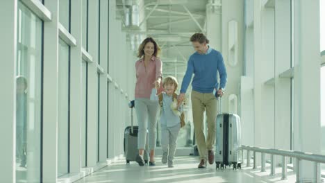 Nice-Cheerful-Mother,-Father-And-Son-Going-Through-The-Passage-In-The-Airport-With-Suitcases-On-The-Wheels-To-The-Plane-As-Having-Vacations-Tour