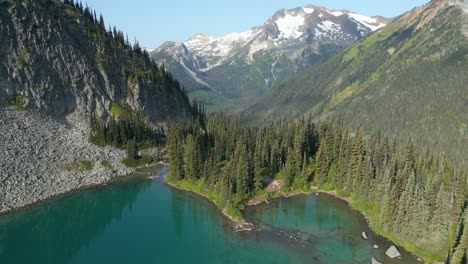 Flying-above-the-turquoise-lake-towards-the-end-of-the-ridge-revealing-green-valley-among-towering-mountains