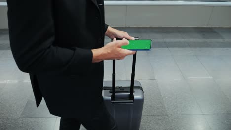 A businessman holding a smartphone with green screen while carrying a suitcase