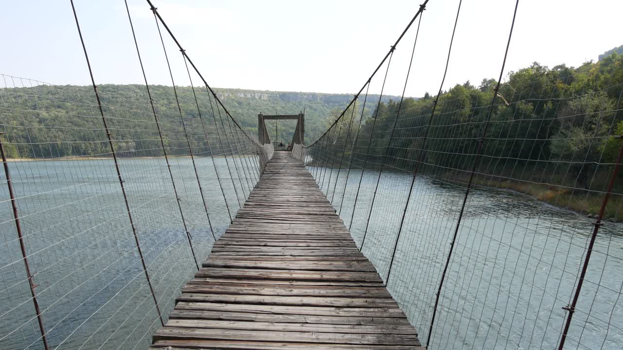 Rope bridge with wooden decking over the mountain river.