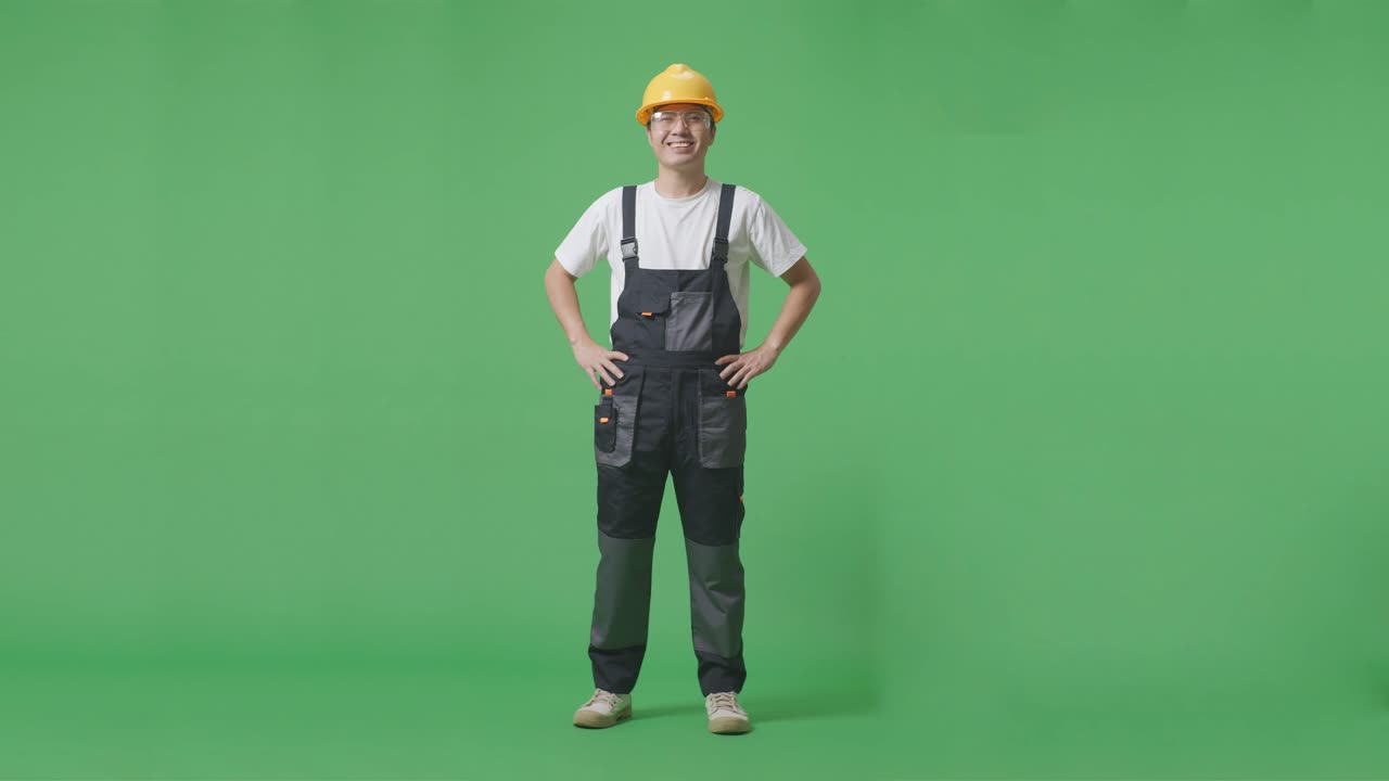 Full Body Of Asian Man Worker Wearing Goggles And Safety Helmet Standing With Arms Akimbo Looking At Camera And Smiling In The Green Screen Background Studio