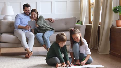 happy young couple watching funny movie while small children draw.