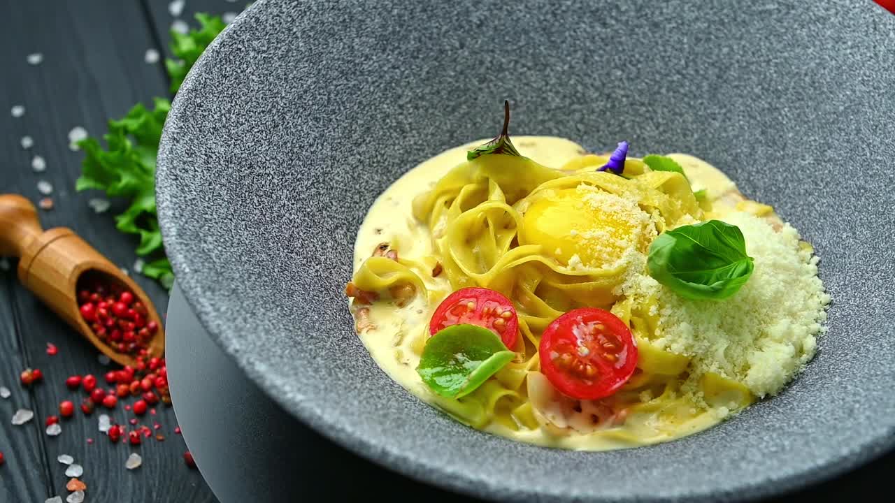 Piatto di pasta con salsa, uovo e pomodorini servito in una ciotola su un tavolo. Una ciotola rotonda contiene pasta ricoperta di salsa cremosa, guarnita con un uovo e pomodorini.