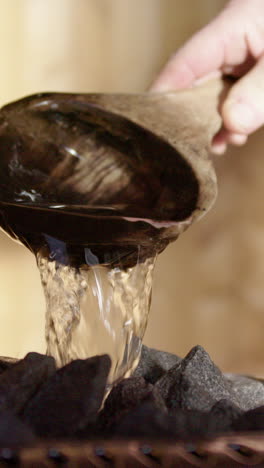 Water poured on heated rocks of stove in wooden sauna, wellness ritual. Vertical