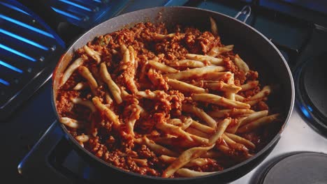 Statische-Nahaufnahme-Einer-Heißen,-Dampfenden-Vegetarischen-Bolognese-Mit-Fileja-Nudeln,-Die-In-Einer-Beschichteten-Bratpfanne-Auf-Einem-Kochfeld-Mit-Filmischer-Zweifarbiger-Beleuchtung-Gekocht-Wird,-Langsames-Zoomen