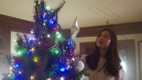 a woman placing a star on top of a christmas tree