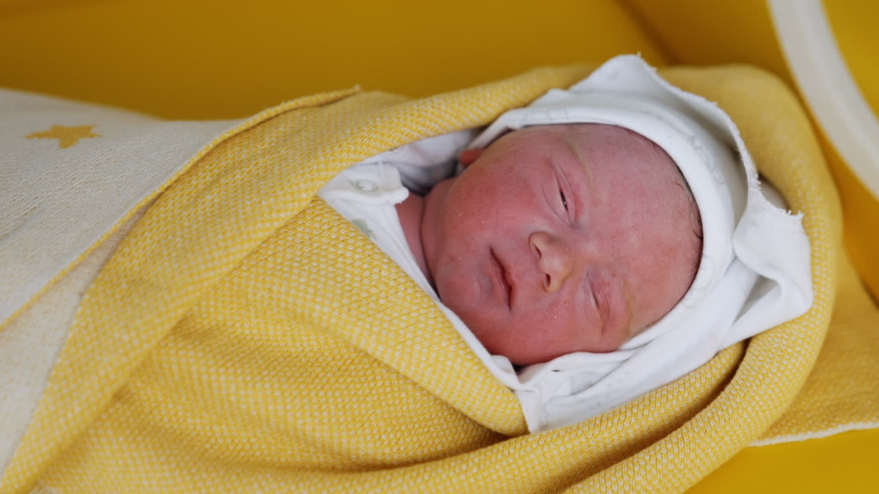 Lovely face of a sleeping newborn coated in blankets. Gloved medic's hands covering the baby after birth. Close up.