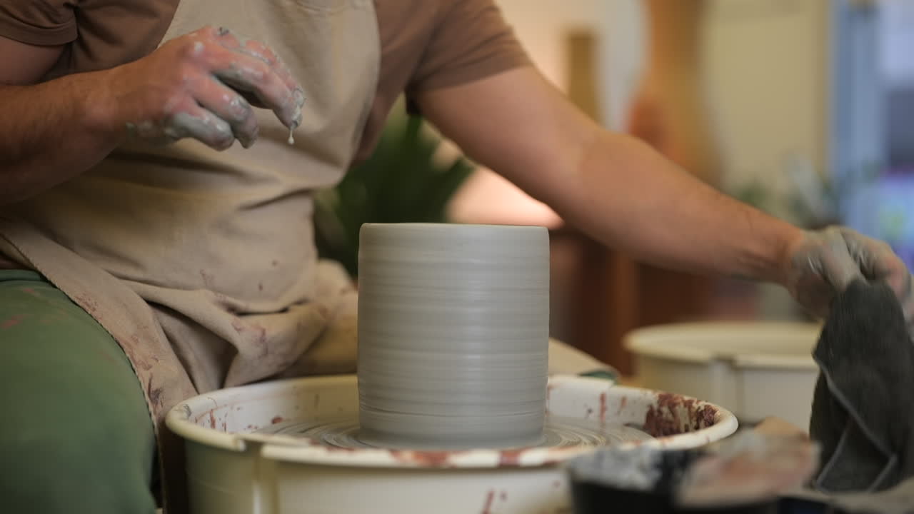 Male potter hands working wet clay on pottery turntable in studio workshop close up