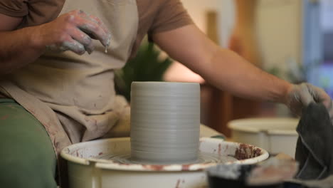 Manos-De-Alfarero-Masculino-Trabajando-Arcilla-Húmeda-En-El-Plato-Giratorio-De-Cerámica-En-El-Taller-De-Estudio-De-Cerca