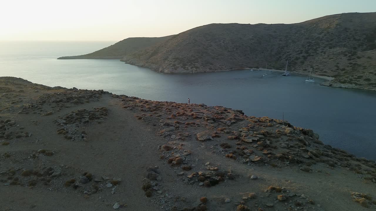 Lone drone pilot standing on island ridge near sun lit ocean