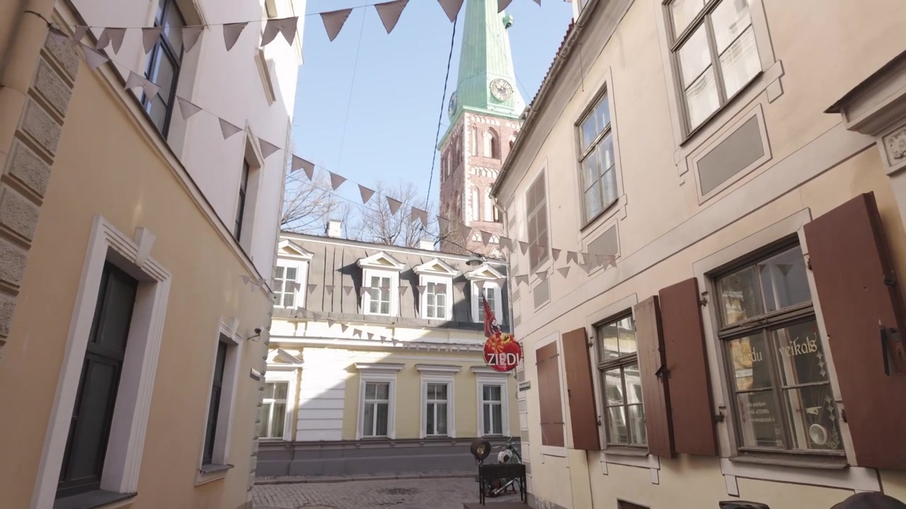 POV segue una donna che porta un caffè da asporto prima che la telecamera riveli la Città Vecchia di Riga