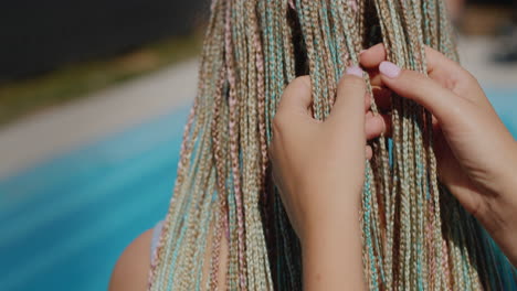una mujer admira las trenzas afro de su hija, las sostiene en su mano. de pie junto a la piscina.4k video