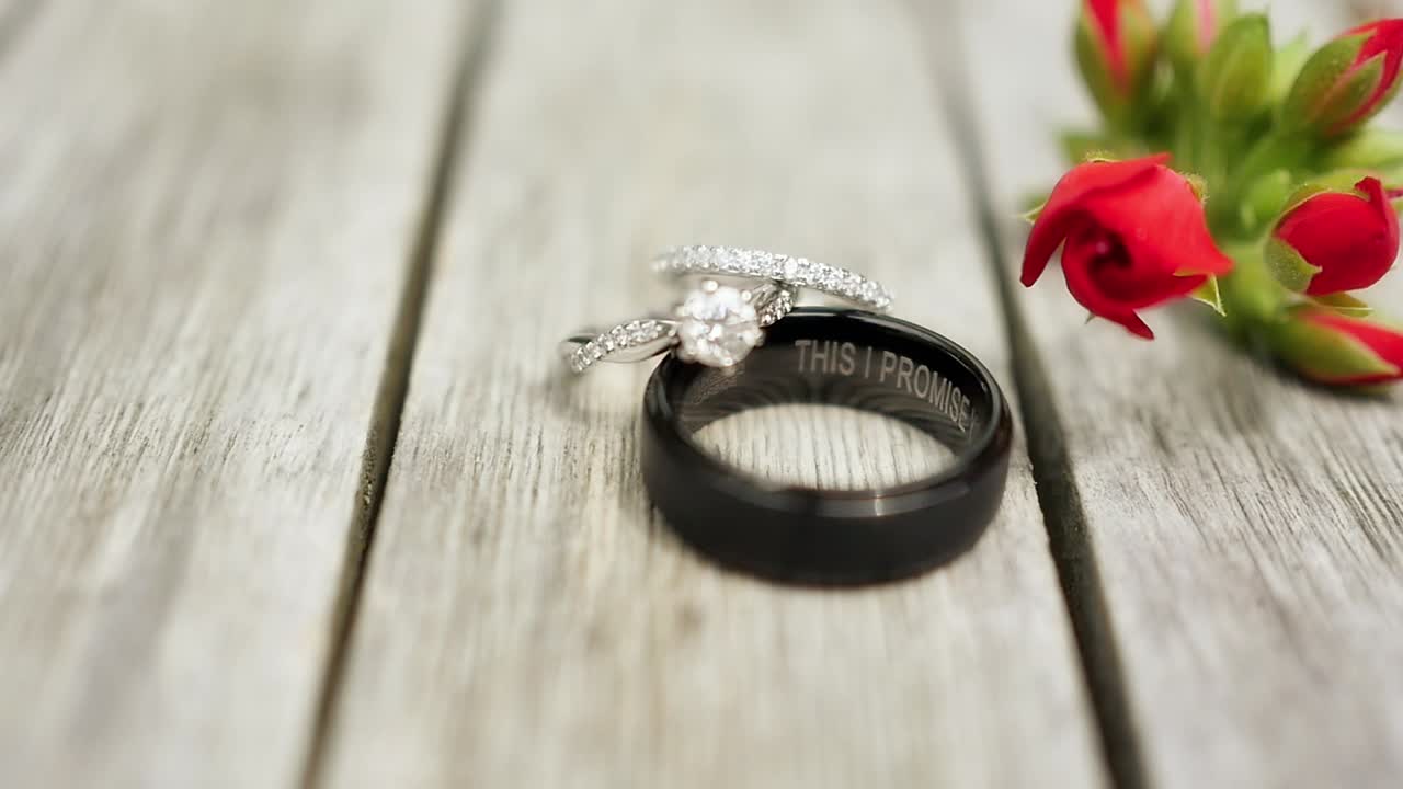 照片中,一位女士的白金订婚戒指和婚戒指在她新丈夫的黑色婚戒指上,上面有"我答应"的文字.