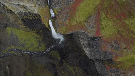 Luftaufnahme-Von-Oben-Nach-Unten-Eines-Fallenden-Wasserfalls-Entlang-Moosiger-Felsiger-Berge-Auf-Der-Insel-Island-–-Schwenkaufnahme