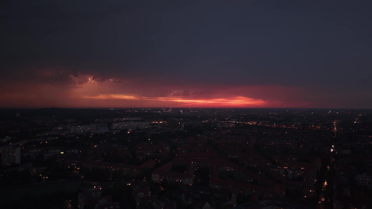Město s viditelným úderem blesku proti bouřkové obloze, osvětlující městskou krajinu v noci. Pěkný letecký panoramatický záběr z dronu shora.