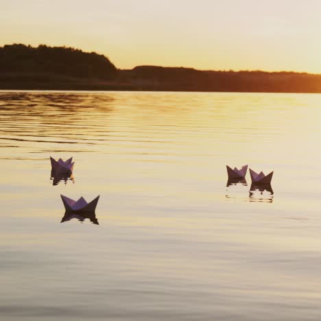 six origami in the form of boats sail by the lake at sunset in the evening. paper boats are drifting with the flow of water far away