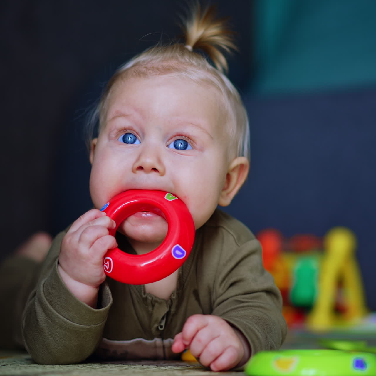 Adorable chubby infant lies on the floor on belly. Lovely baby chews the toy, looks up and smiles. Close up