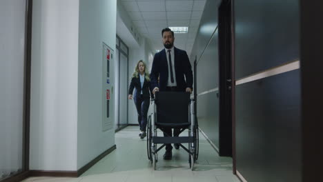 businesspeople pushing wheelchair in office corridor
