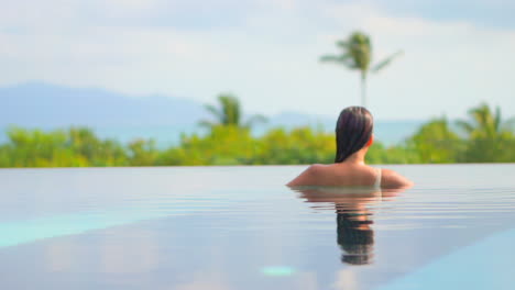 back of sexy exotic woman in infinity pool enjoying in water, view of a tropical landscape on hot summer day, slow motion full frame
