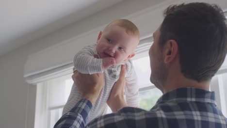 loving father lifting smiling baby son in the air and playing game at home together - shot in low motion