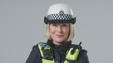 studio portrait of smiling mature female police officer against plain background