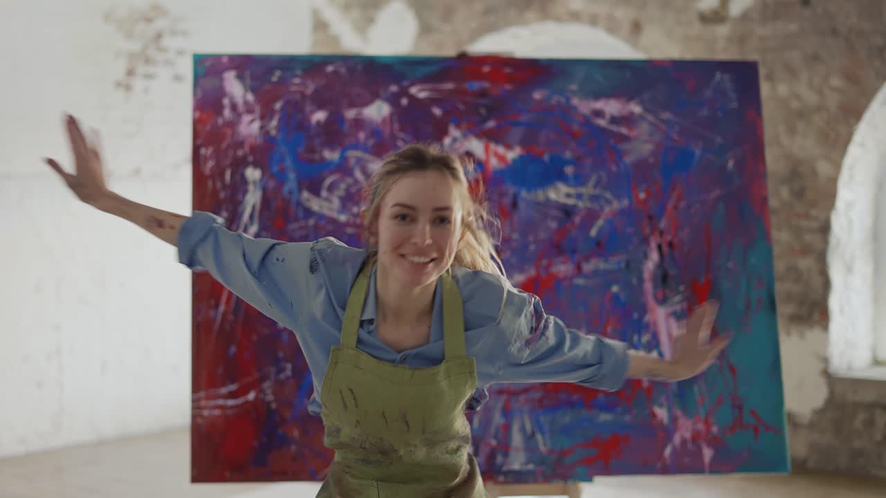 여성 예술가 가 스튜디오 에서 추상화 앞 에서 감정적 으로 춤 을 추고 있다