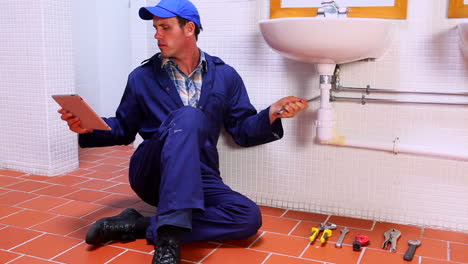 handsome plumber fixing sink and checking tablet pc