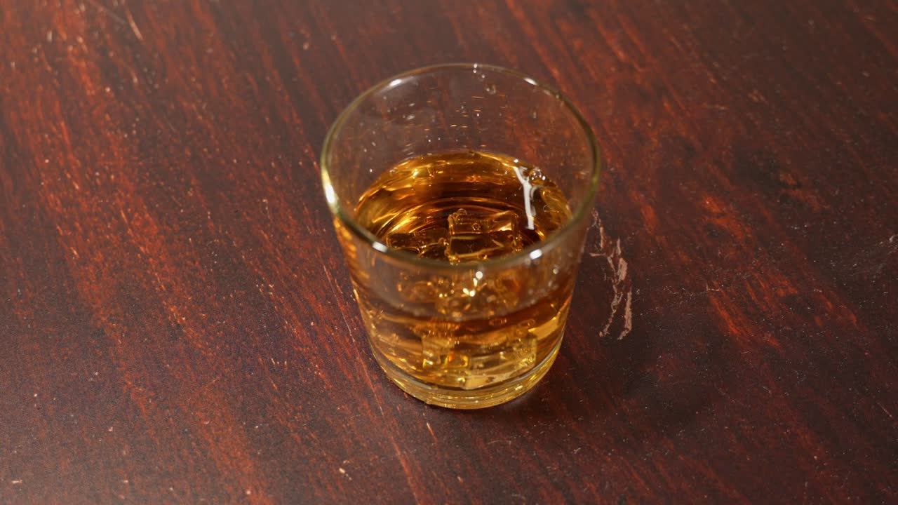 A pour of whiskey swirls into a glass, the amber tones reflecting soft light against the tabletop