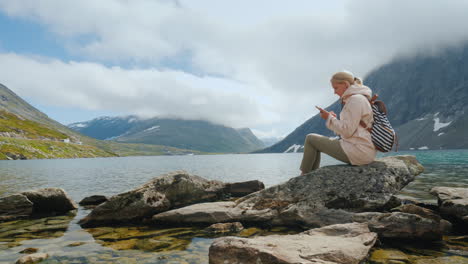 a traveler uses a smartphone high in the mountains near the highland norwegian lake successful woman