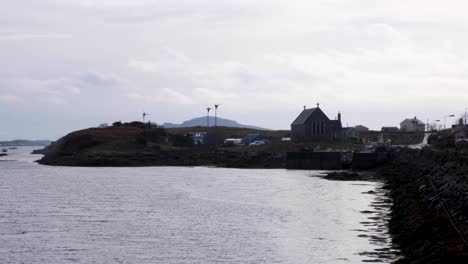 Vista-Costera-De-Una-Iglesia-Y-Turbinas-Eólicas-Junto-Al-Océano-En-La-Isla-De-Barra-En-Las-Hébridas-Exteriores-De-Escocia,-Reino-Unido