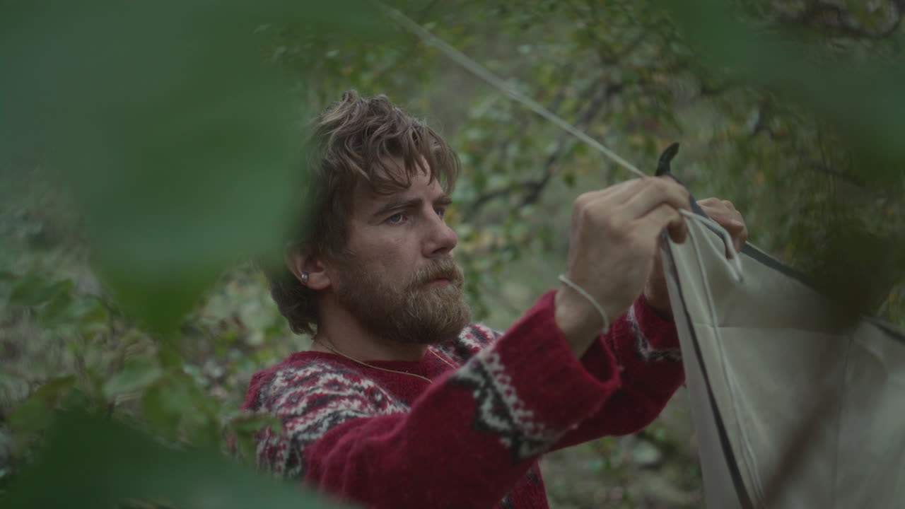 Survivalist Adjusting Camping Tent on Rope between Trees in Forest