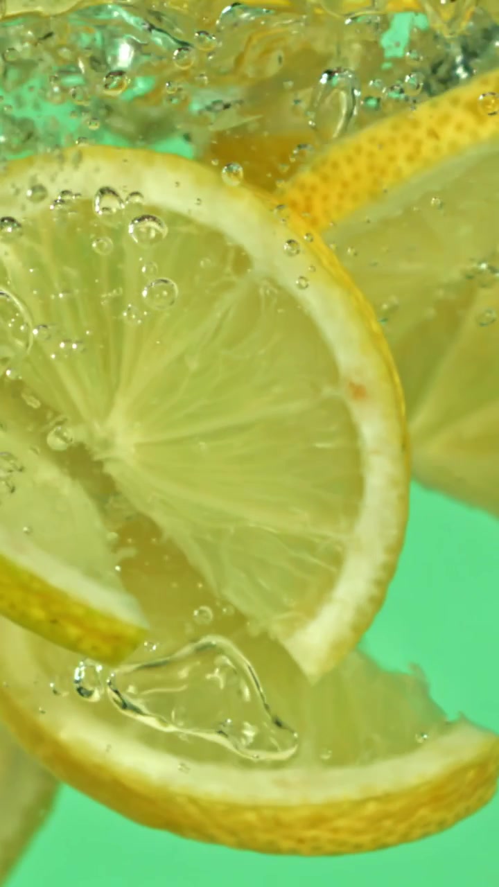 Fette di limone che cadono al rallentatore nell'acqua con bolle