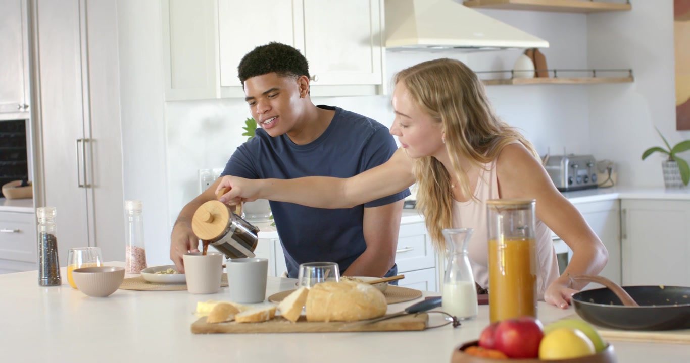 Coppia, donna in canotta che si protende sull'isola della cucina, versa caffè dalla caffettiera a stantuffo per colazione.