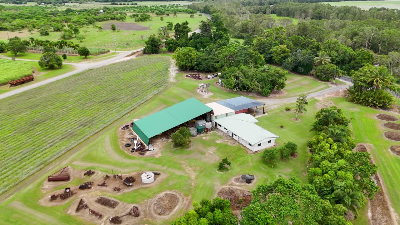 Drone footage captures a lush sugarcane farm in Port Douglas, Queensland, showcasing green fields and farm structures under overcast skies