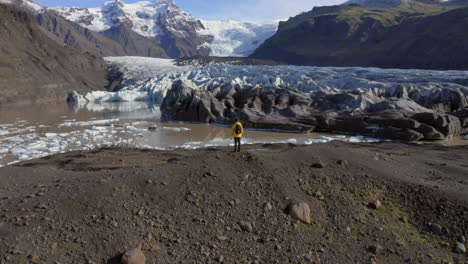 Luftaufnahme:-Langsame-Schwenkaufnahme-Eines-Mannes,-Der-An-Einem-Sonnigen-Tag-Still-Auf-Einem-Hügel-In-Der-Nähe-Des-Svinafellsjökull-Gletschers-Steht