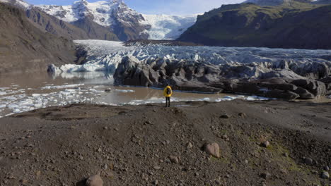 antena: toma panorámica lenta de un hombre parado en una colina cerca del glaciar svinafellsjokull durante un día soleado