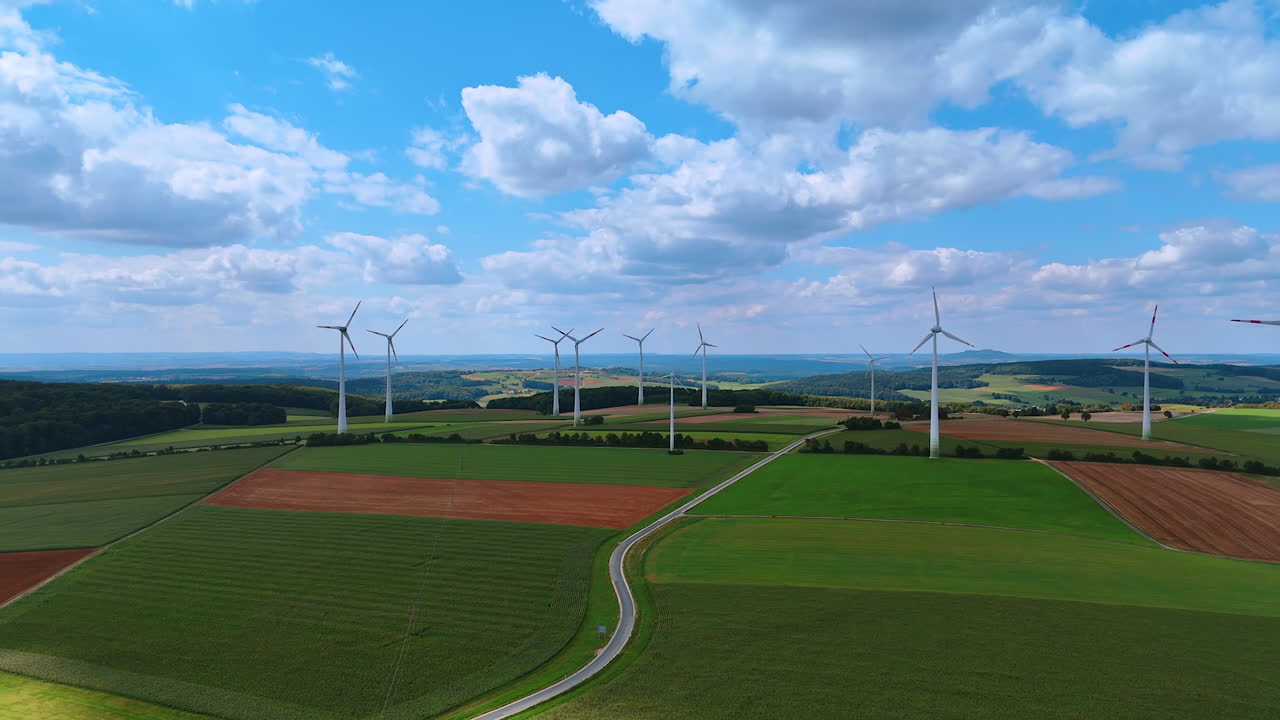 Flight above the beautiful green fields crossed by the highway. Windfarm produces sustainable energy in the countryside