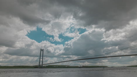 Zeitraffer-Mit-Bewölktem-Himmel-Auf-Einer-Hohen-Hängebrücke-über-Einem-Großen-Fluss,-HDR