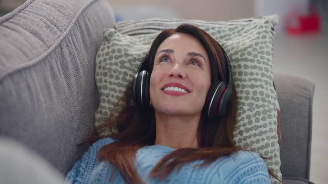 소파 에 헤드폰 을 들고 음악 을 듣고 있는 미소 짓는 여자