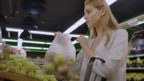 mujer de mediana edad pesa una bolsa de manzanas en el supermercado