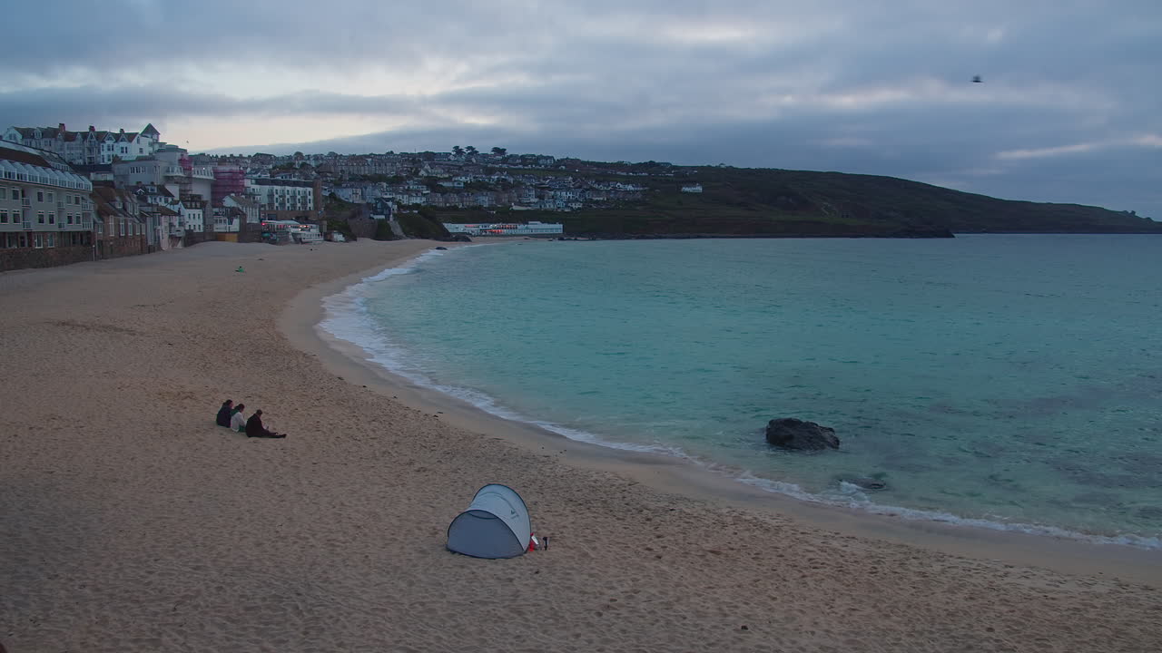 People Sat On The Sandy Shore With Tent On Porthmeor Beach In St Ives, England. Aerial Wide Shot
