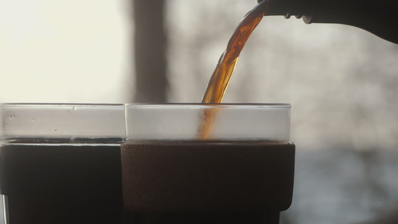 Pouring steaming hot coffee from a thermos flask into a sustainable keep cup out of glass. Early Morning in the forest outdoors. Environment Friendly 4KClose Up