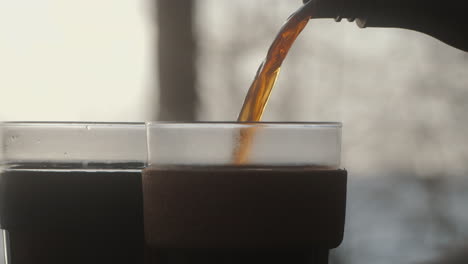 pouring steaming hot coffee from a thermos flask into a sustainable keep cup out of glass. early morning in the forest outdoors. environment friendly 4kclose up