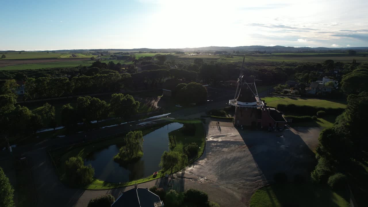 forward movement with drone towards the sunset and showing a beautiful Dutch windmill next to it