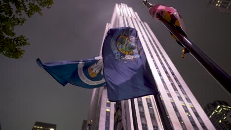 looking up at rockefeller center building with flags at night