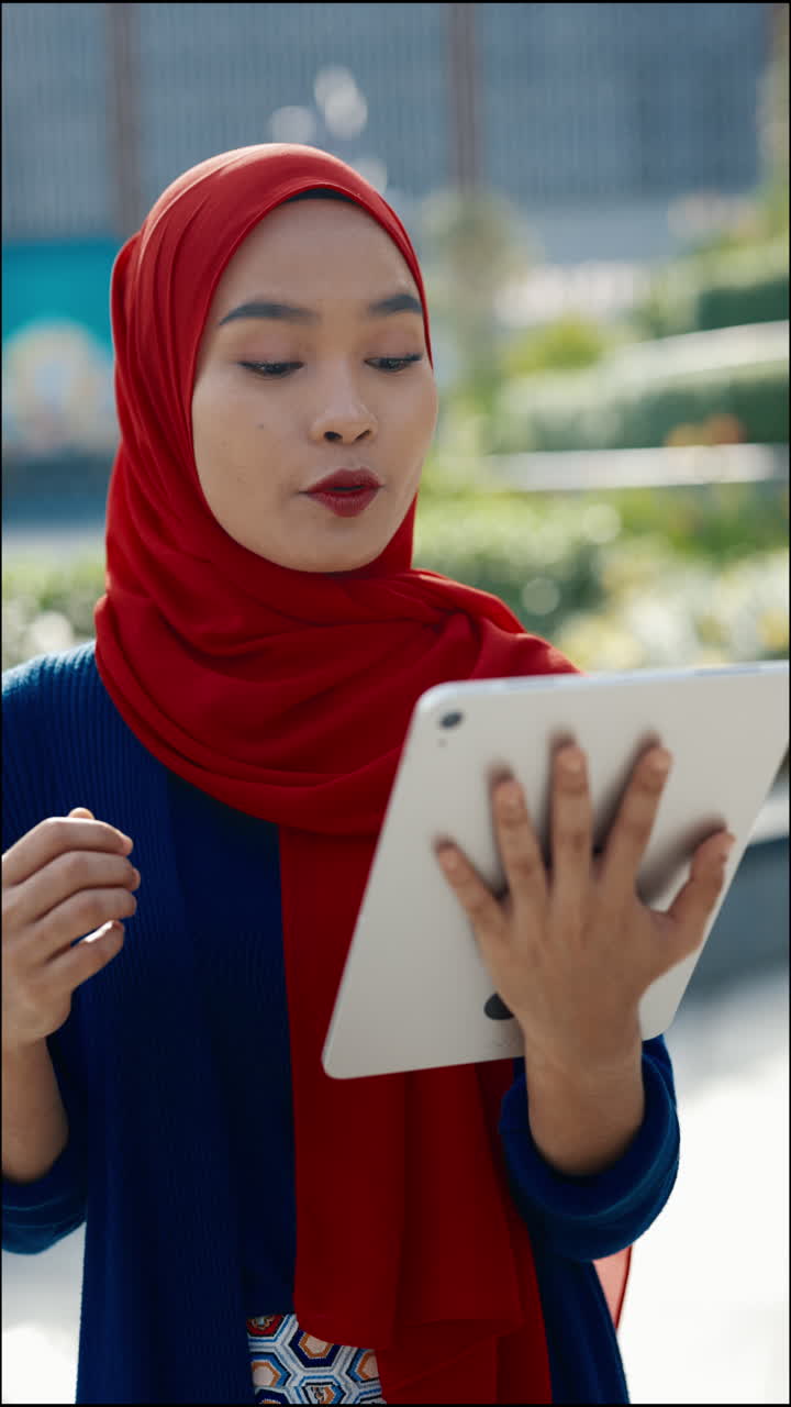 Young Muslim Woman in Red Hijab Using a Tablet Outdoors