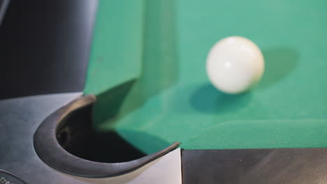 up view of black billiard ball rolling toward pool pocket after being struck by white cue ball on green felt table. close-up captures motion, precision, and dynamics of billiards gameplay